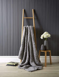Grey knitted blanket draped over a wooden ladder against a dark paneled wall.