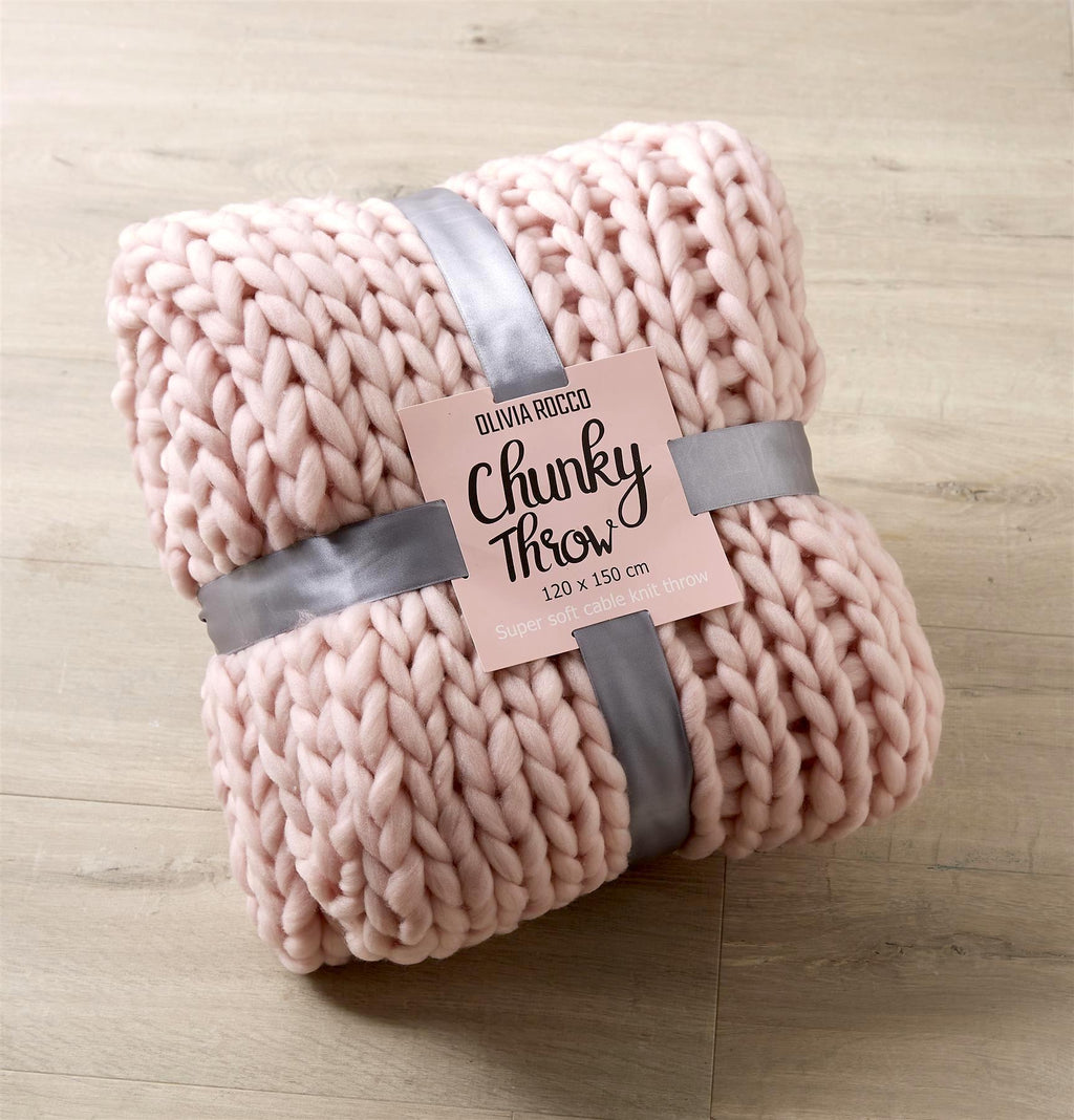 Pink chunky throw blanket with a label on a wooden surface