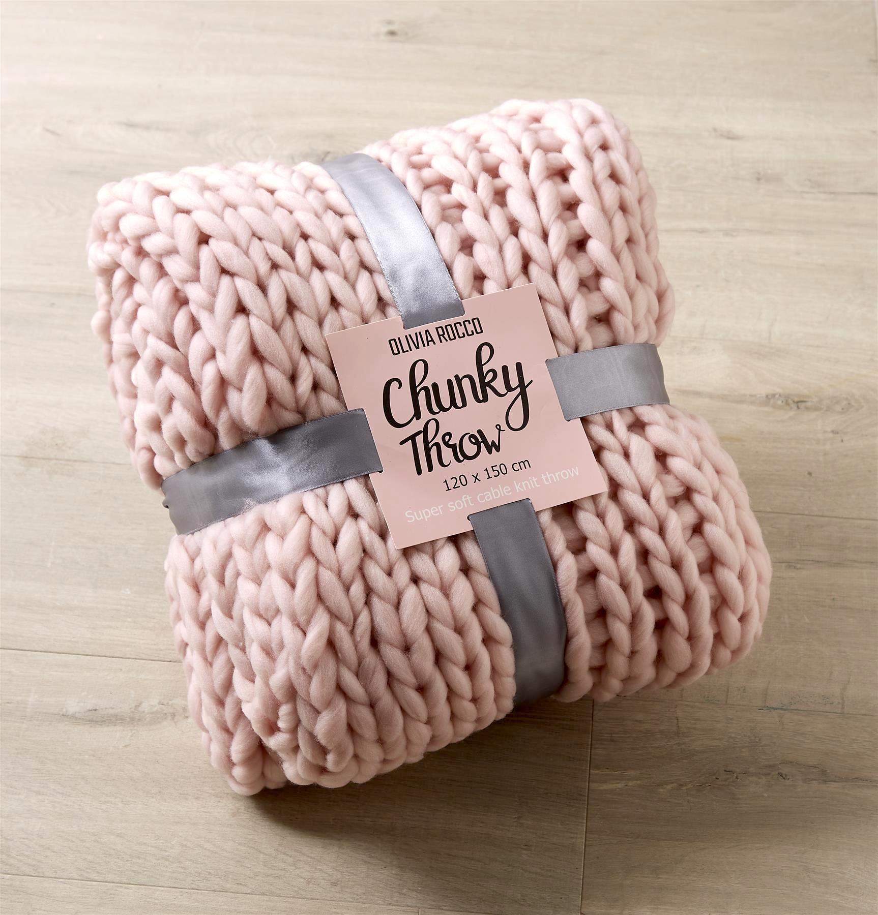 Pink chunky throw blanket with a label on a wooden surface