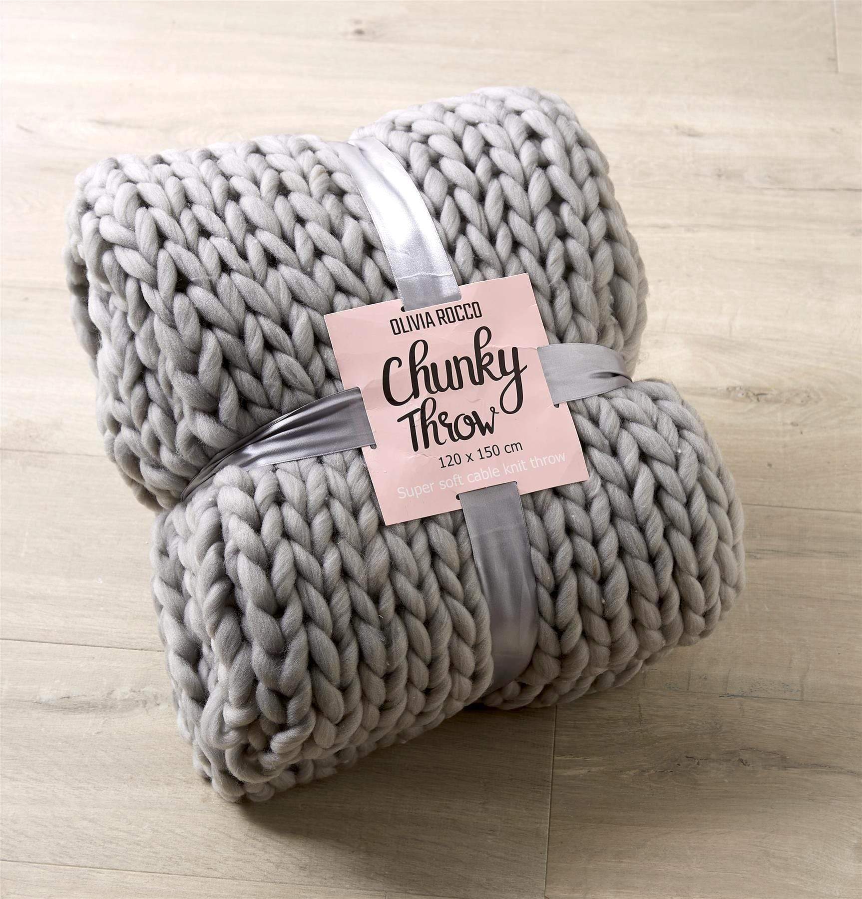 Grey chunky knit throw blanket with a label on a wooden surface