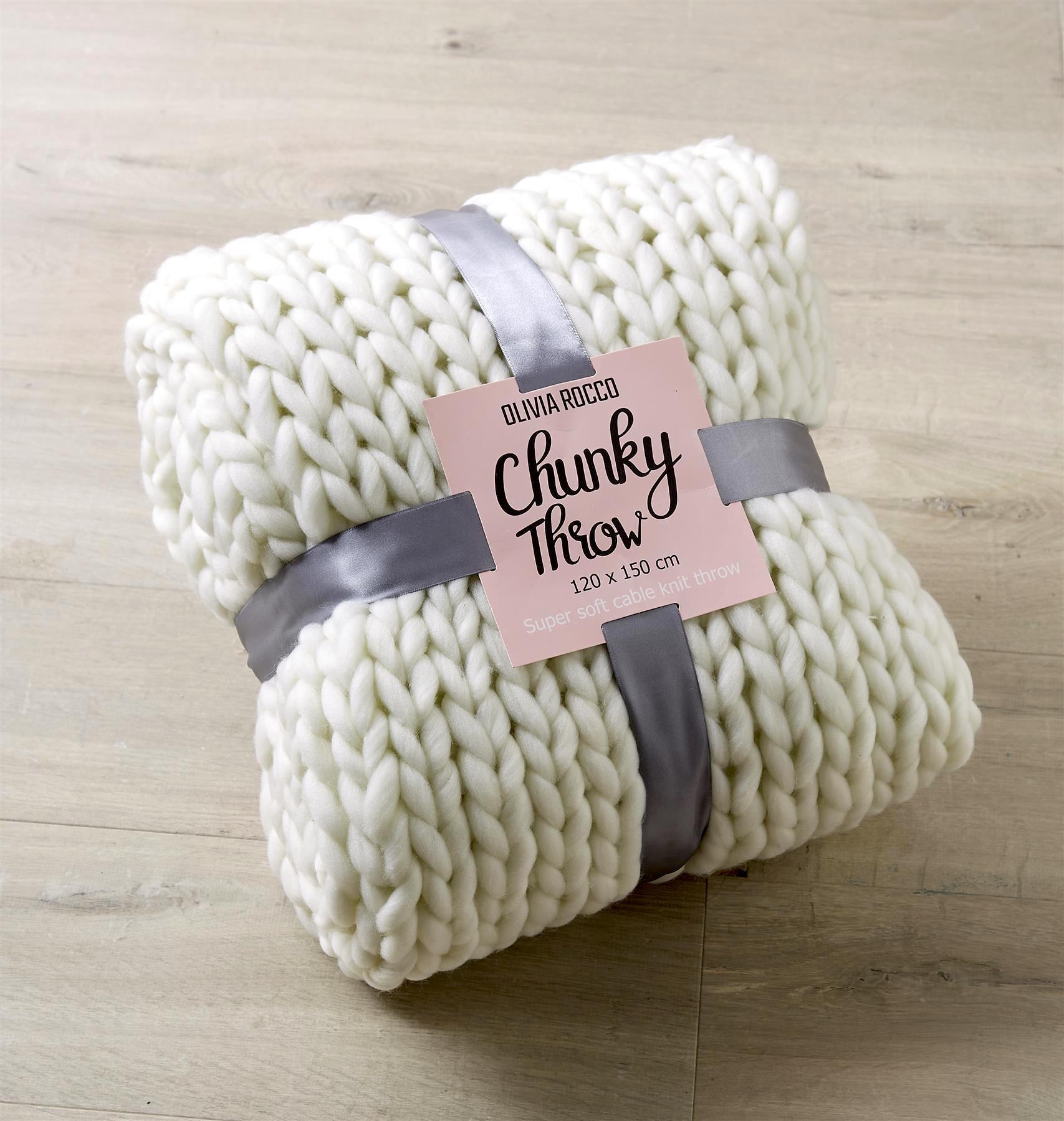 White chunky knit throw blanket with a label on a wooden surface
